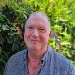 Photo of man with short brown hair in front of brick wall