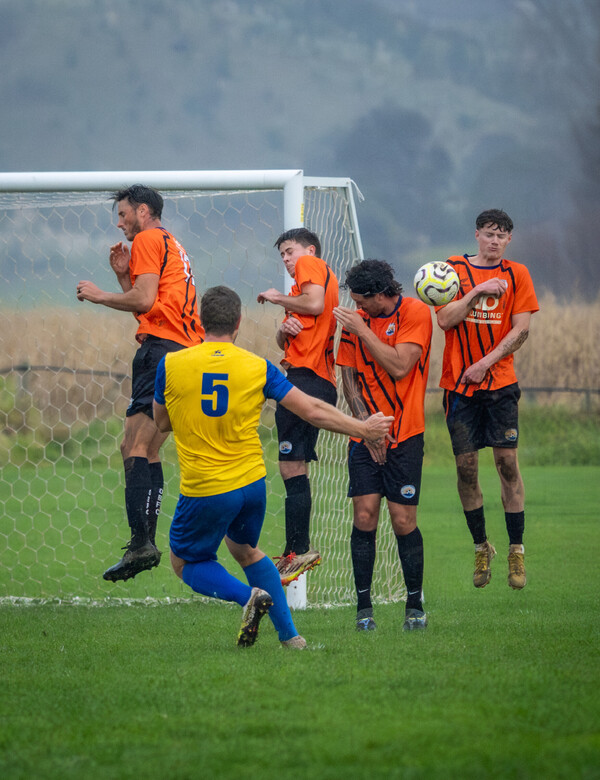 Sports action photo of footballer taking a free kick into a wall of opposition players at a season game in Ohope, New Zealand.