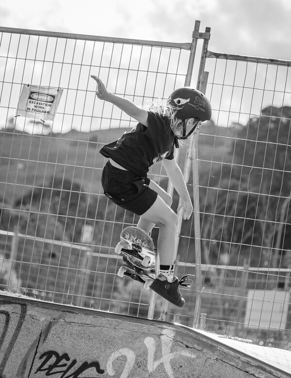 Black and white portrait of a young skateboarder mid-jump with construction in background. 