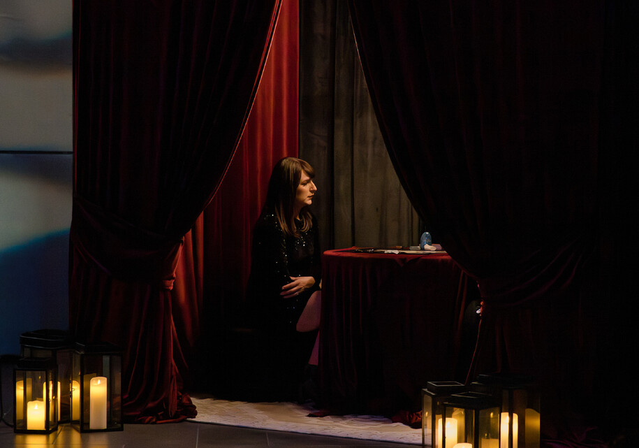 Moody event photo of a guest in a red velvet tarot card reading tent with candles outside.