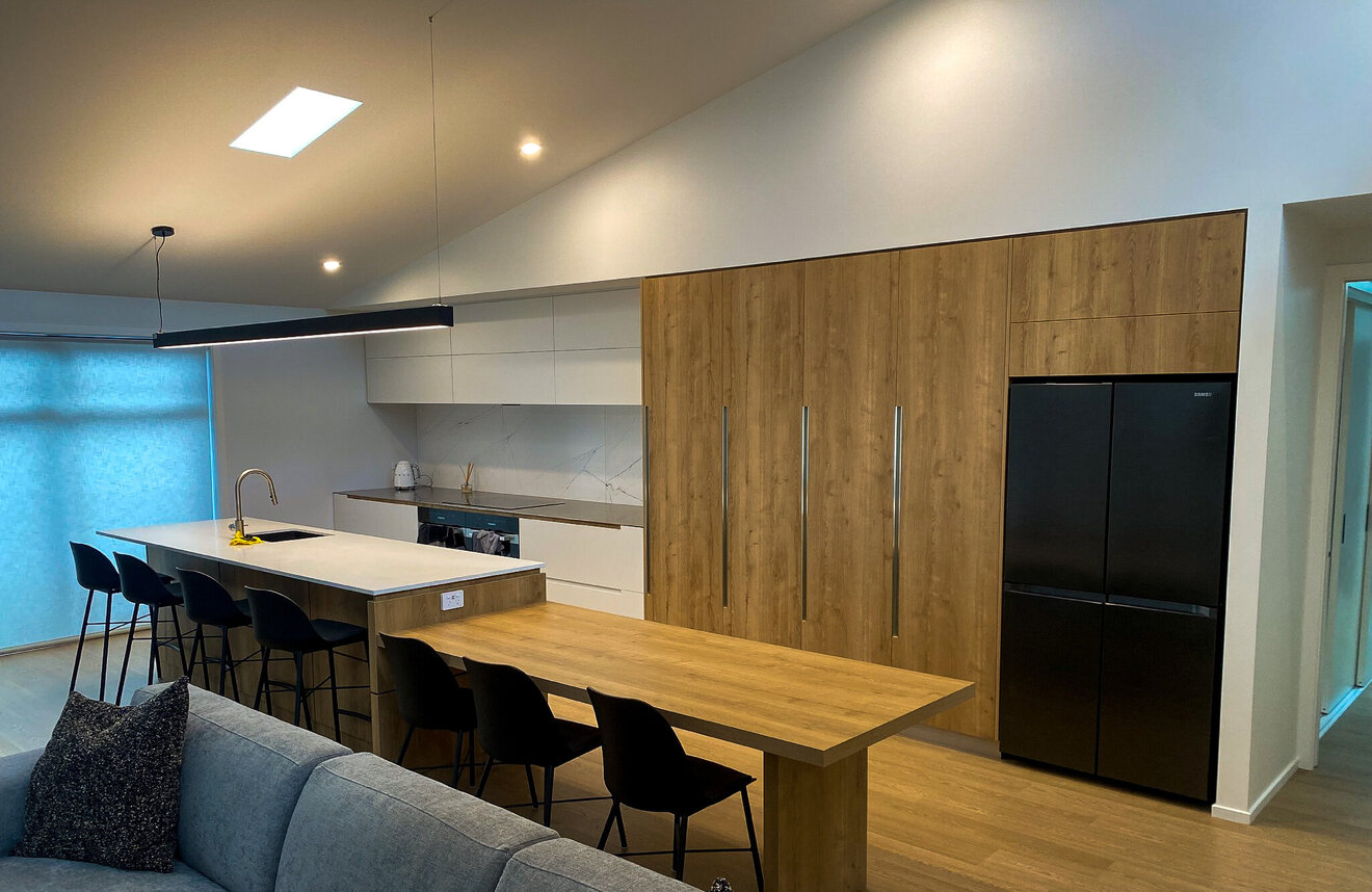 Hero image of a sleek modern kitchen with integrated appliances, large island, and custom joinery by Barrett Joinery in Timaru.