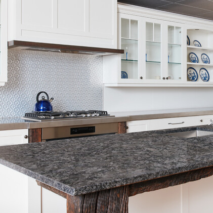 Elegant white kitchen design with glass-front cabinets and a polished stone benchtop, showcased in Barrett Joinery's Timaru showroom to illustrate premium joinery and tailored design.