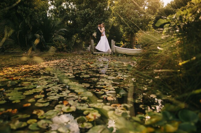 Wedding couple standing on the jetty overlooking pebble beach at Markovina Estate in Kumeu