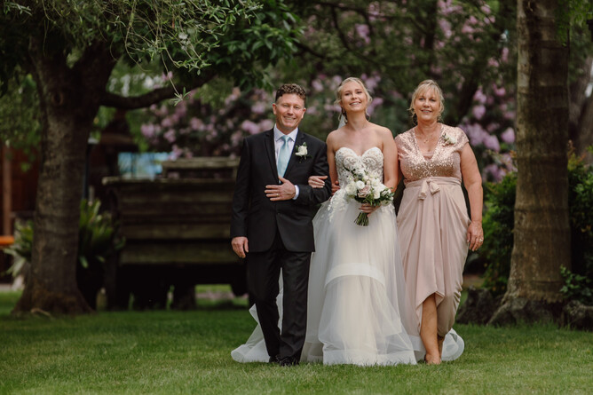 Parents of the bride walking her towards the wedding ceremony aisle at Markovina Estate in Kumeu