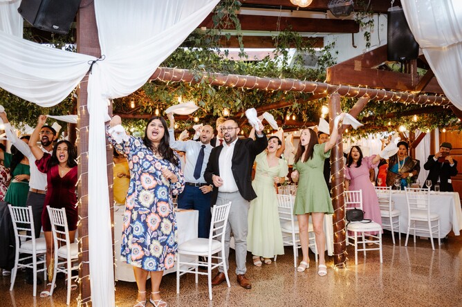 Wedding guests celebrating by raising napkin during the wedding reception at Markovina Estate in Kumeu