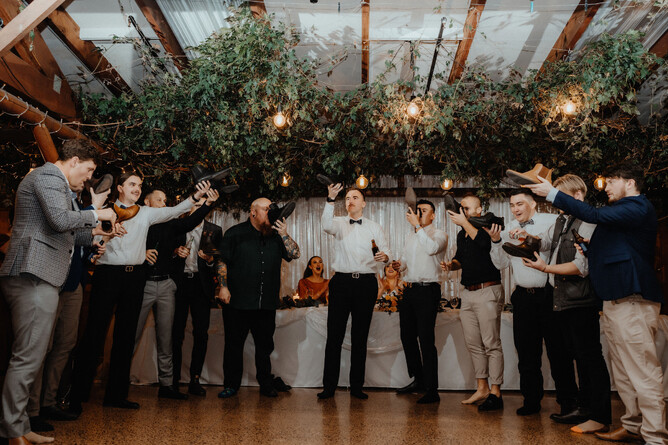 Groomsmen celebrating wedding by drinking from a shoe during the reception at Markovina Estate in Kumeu
