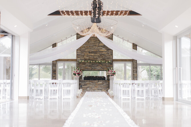 White indoor wedding ceremony setup at the stone fireplace at Markovina Estate in Kumeu