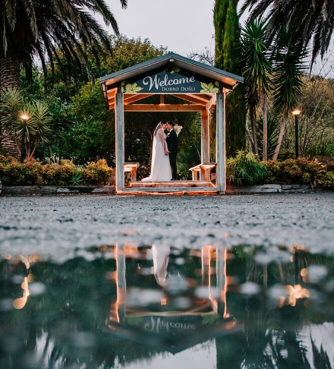 Bride & Groom Photo at Welcome Sign in Rain at Markovina Vineyard Estate in Kumeu