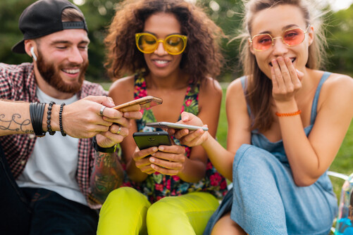Photo of three people looking sharing their phone screens with each other.