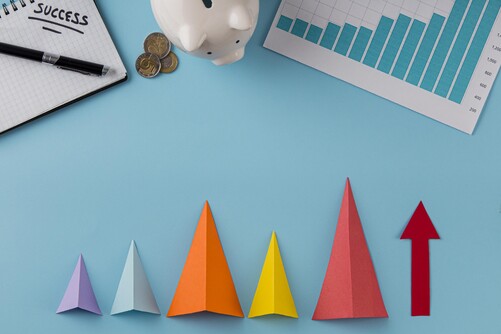 Photo of sticky notes in a variety of colours folded into triangular paper planes, lined up to resemble a bar graph indicating growth.