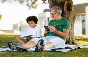 Man and child reading under a tree on a sunny day