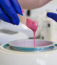 Hands in disposible gloves holding a stick with wax dripping off it back into the wax pot
