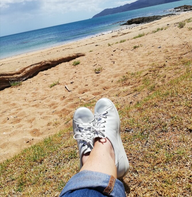 Woman sitting at a beach looking out at an island.