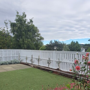 White fence enclosing backyard with artificial lawn and garden beds