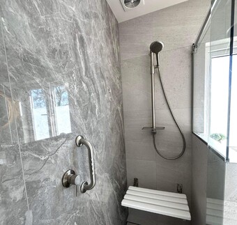 Accessible shower with stylish tiles, built-in seat, and stainless steel grab rail for safety