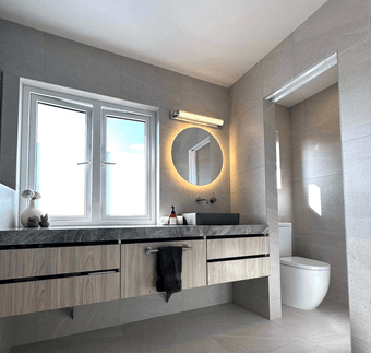 Bathroom renovation featuring a modern vanity with a round mirror light and a separate toilet visible in the background