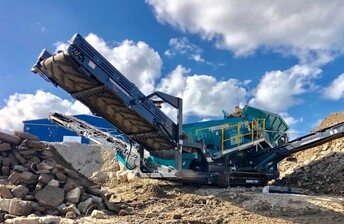 closeup of conveyor arm of Powerscreen Warrior 1800 screening machine working in yard processing waste concrete that has been crushed