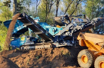 Powerscreen Warrior 1200 screen machine working in a forest to process soil into grades and being loaded by a moxy tip  truck