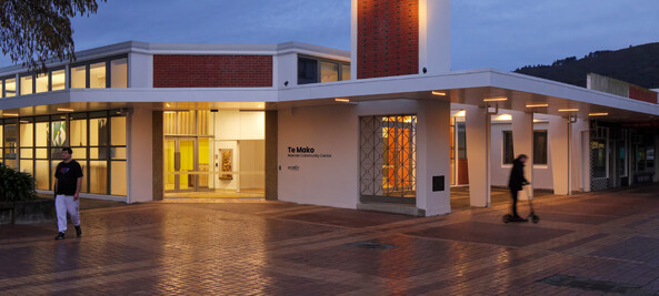 A photo of Te Mako from outside in the evening, the lights are shining through the front doors.