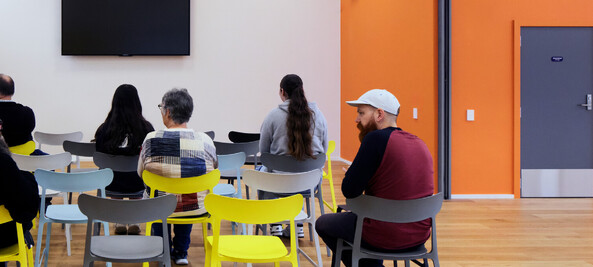 picture from behind of people using one of our activity rooms. There is a wall mounted TV in the background.