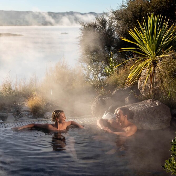 Couple relaxing in a natural thermal pool at Polynesian Spa in Rotorua, New Zealand, with lake views