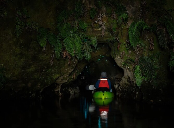 Kayak approaching the entrance of a dark glow worm cave in Rotorua at night