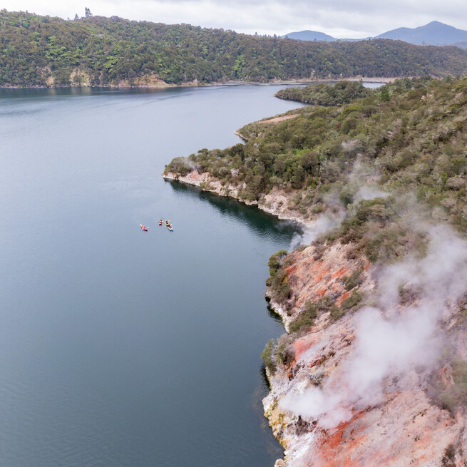 Kayaks on Lake Rotomahana with colour landscapes