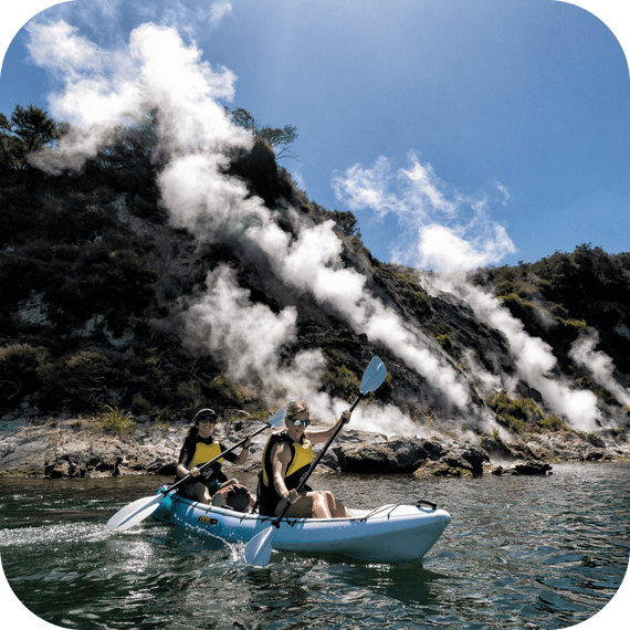 Kayakers on Lake Rotomahana in Waimangu Valley paddling past steaming geothermal cliffs