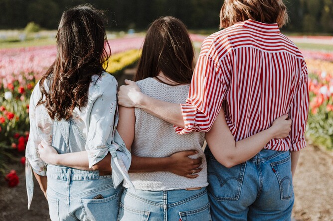 Three women standing together with arms around each other, symbolising board diversity