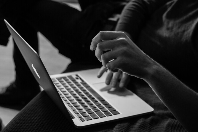 A black and white image of a person typing on a laptop, hands in focus