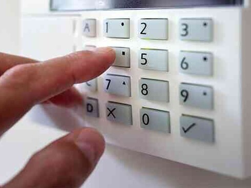 an alarm keypad with a hand in view.