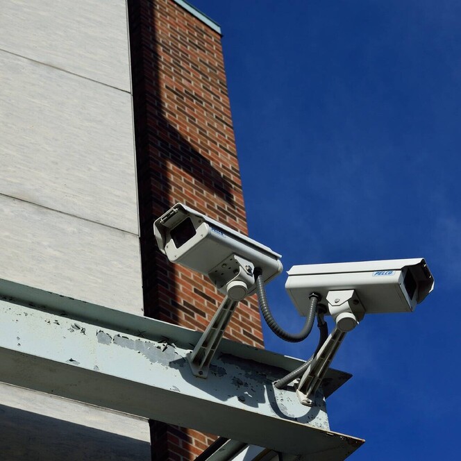 A photo showing 2CCTV cameras installed on metal framework on the side of a commercial brick and stone building.