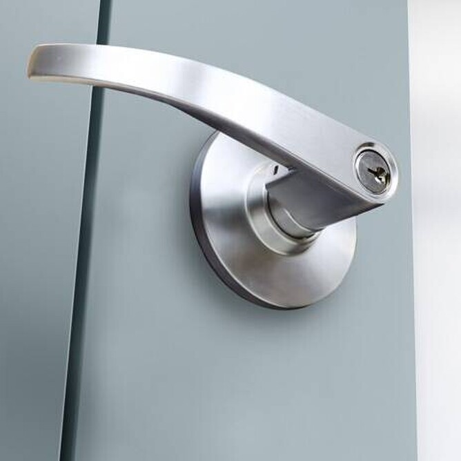 a picture of a partially open grey door, showing a brushed chrome doorhandle with lock insert.