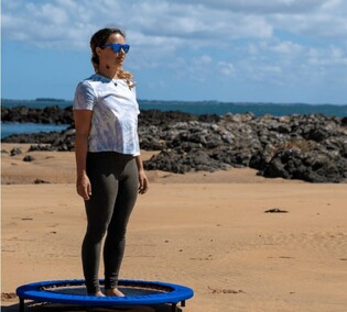 Woman on a XenPod Lymphaciser wellness mini-trampoline at the beach