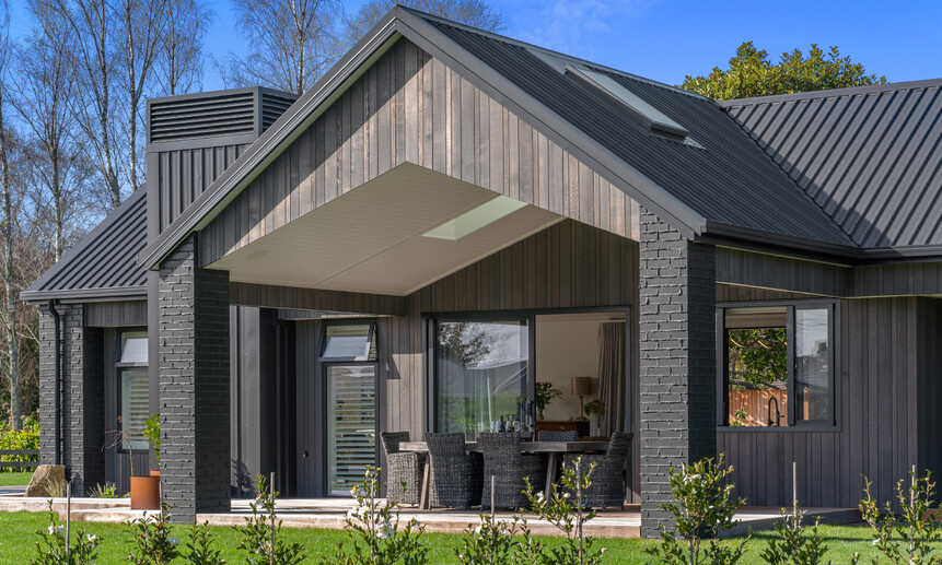 Bold black exterior makes this custom home stand out, featuring a roofed outdoor entertaining area and a wooden gable.