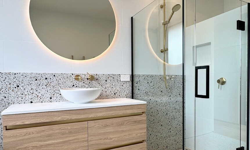 Circular lit mirror and glass shower walls keep this bathroom light, open and elegant in this designer home.