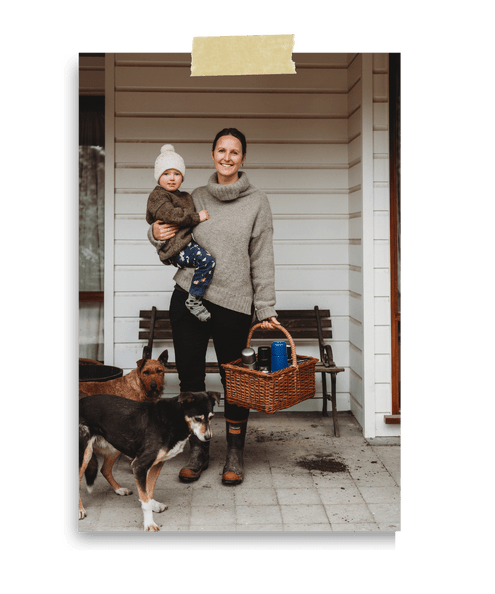 Jaz Mathisen holding her child with a basket in her hand and two working dogs at her feet.