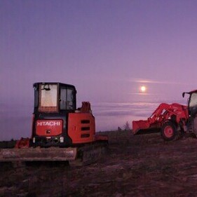 Hitachi digger, red tractor, and trailer parked at a hillside earthworks site at dusk – North Canterbury civil works contractors in action.