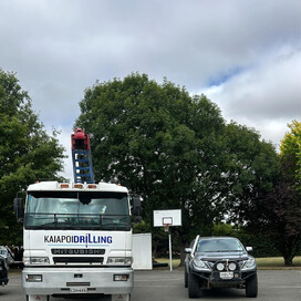 Front view of a Kaiapoi Drilling Mitsubishi truck parked beside a ute on asphalt with “First hole for the year done 🤘 onto the next” caption – drilling services North Canterbury.