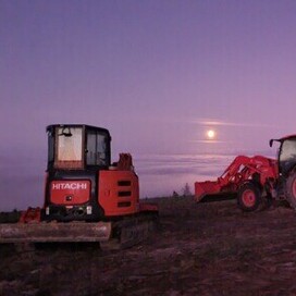 Hitachi digger, red tractor, and trailer parked at a hillside earthworks site at dusk – North Canterbury civil works contractors in action.