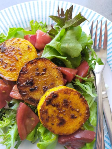 Cooked Courgette rounds with lettuce and tomatoes on a blue and white plate