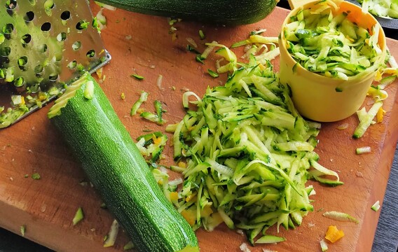 grater and grated courgette on wooden chopping board