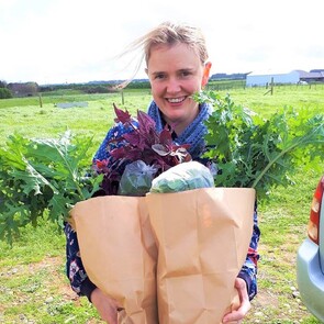 Smiling woman holding paper bags overflowing with vegetables