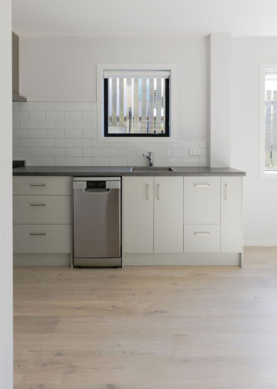 A dark grey kitchen with green tiles and a heavily textured wood look laminate floor.