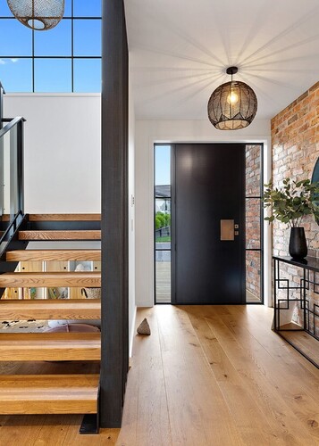 A modern entranceway with black front door, brick wall, wooden stairs and a natural wood floor. 