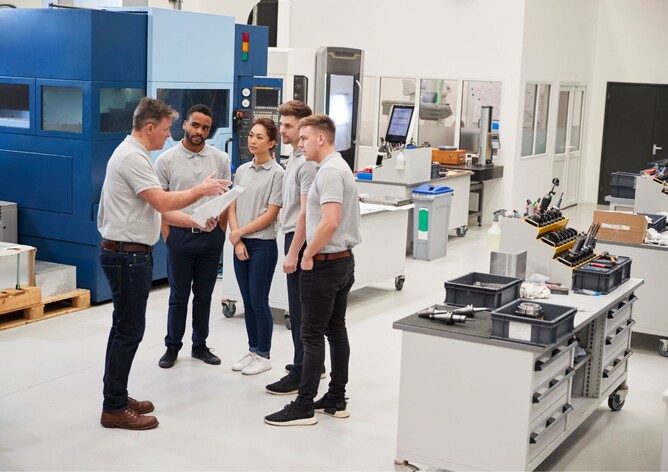 A group of workers in a factory training on the floor by the manager