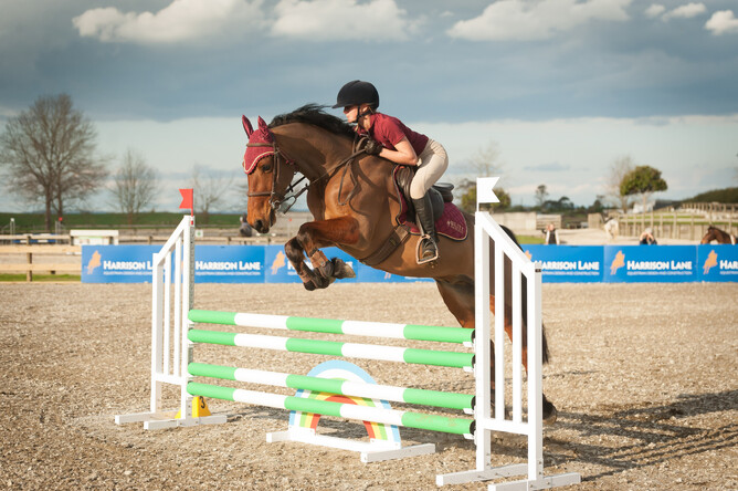 Maddy Cutfield and her horse Watch Me Fly jumping with Harrison Lane signs in the background