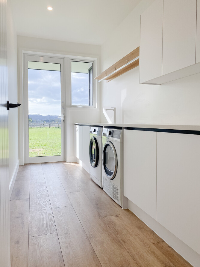 Galley style laundry with wooden flooring and white cabinetry