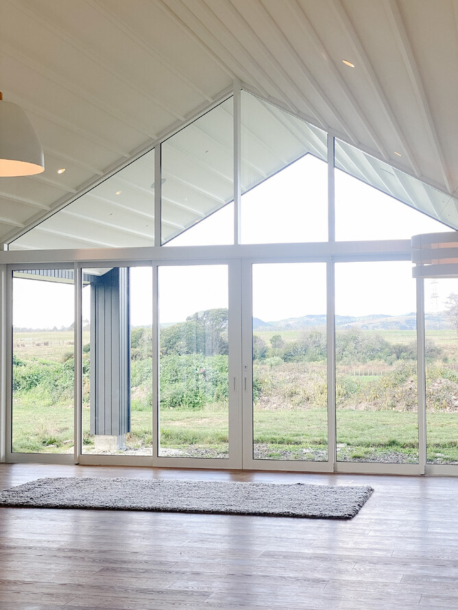A view from living area to an exterior country landscape through a feature gable window