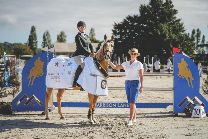 Laura Daly presents Elise Edwards-Smith with the champion rug in front of the Harrison Lane fence.